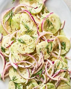 a white plate topped with sliced cucumbers and red onion salad next to a fork