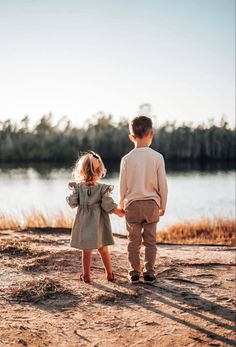 two young children are walking towards the water