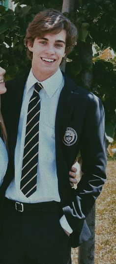 a young man and woman standing next to each other in front of a tree wearing ties