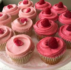 there are many cupcakes with pink frosting and raspberries on top