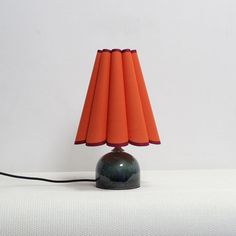 an orange lamp sitting on top of a white bed next to a black and red shade