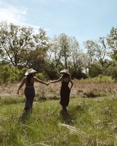 two women are walking through the grass holding hands