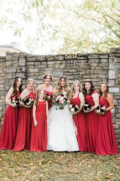 a group of women standing next to each other in front of a stone wall holding bouquets