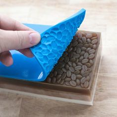 a person holding a blue plastic object with coffee beans in it