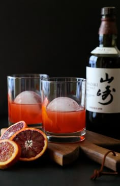 two glasses filled with blood oranges next to a bottle