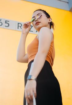 a woman in an orange tank top and black skirt holding a white bag while talking on her cell phone