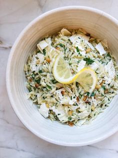 a white bowl filled with pasta and lemon wedges on top of a marble table