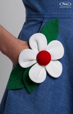 a close up of a person's hand holding a flower brooch with leaves on it