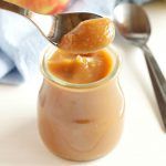 a spoon full of caramel sauce with an apple in the background