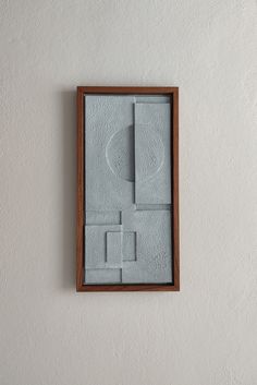 an abstract painting on the wall in a wooden frame with paper squares and rectangles