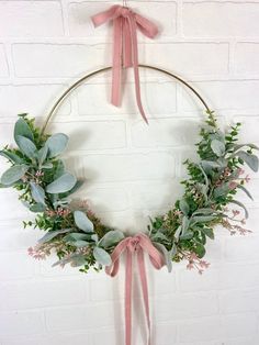 a wreath hanging on the wall with pink ribbon and greenery in front of it