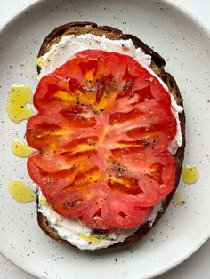 a white plate topped with a piece of bread covered in cheese and tomato slices on top of it