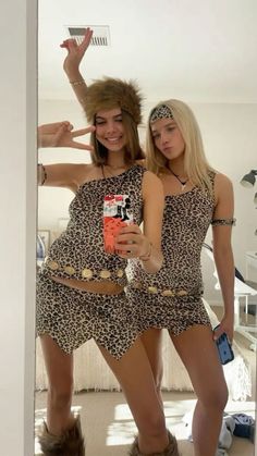 two women dressed in animal print outfits are posing for the camera and one is holding a cell phone