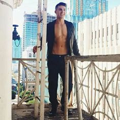 a shirtless man standing on top of a wooden structure in front of tall buildings