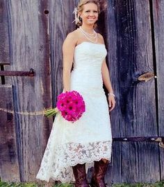 a woman standing in front of a wooden door wearing boots and holding a pink bouquet