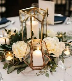 a table with candles and white flowers on it, surrounded by glass vases filled with greenery