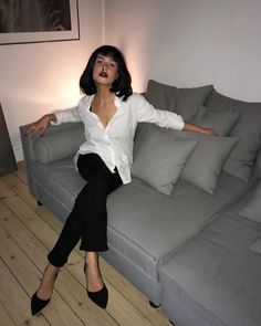 a woman sitting on top of a gray couch next to a white wall and wooden floor