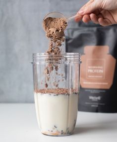 a person is scooping chocolate into a blender filled with milk and cocoa powder