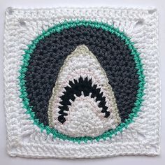 a crocheted square with a shark's teeth on it, in white and green