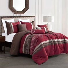 a bed with red and brown comforters in a bedroom next to a mirror on the wall