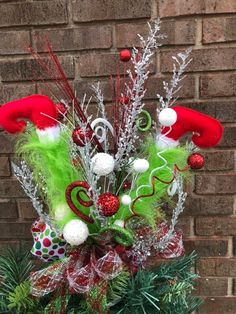 a christmas arrangement in front of a brick wall with green and red decorations on it