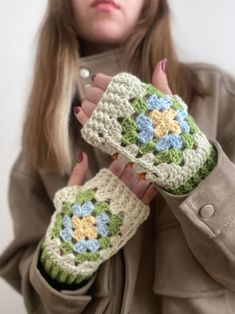 a woman holding two crocheted gloves with flowers on them