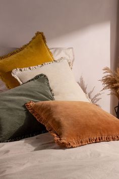 a bed topped with lots of pillows next to a plant