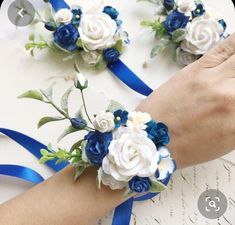 two blue and white flowers are being held by someone's hand on top of a table