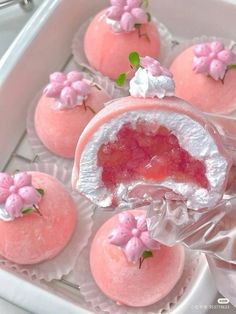 pink desserts with white frosting and flowers on them are in a plastic container