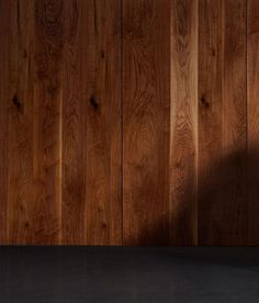 a person standing in front of a wooden wall with their shadow on the floor,