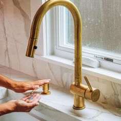 a woman is washing her hands under a faucet in the kitchen sink with marble counter tops