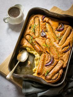 a casserole dish with onions and bread in it next to a cup of coffee