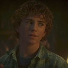 a young man with curly hair wearing a green shirt and looking at the camera while standing in a dark room