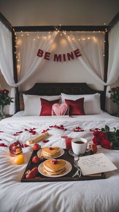 a bed topped with lots of white sheets covered in red rose petals and plates filled with pancakes