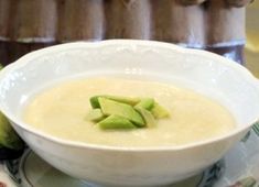 a white bowl filled with soup on top of a plate next to an apple slice