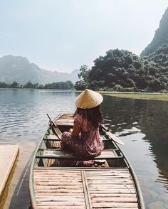 a woman in a straw hat is rowing a boat on the water with mountains in the background