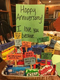 a basket filled with lots of candy sitting on top of a table next to a sign that says happy anniversary i love you because