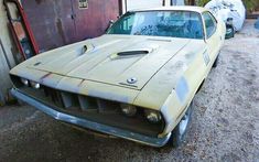 an old yellow car parked in front of a garage door with rust on the hood