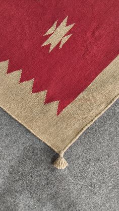 a red and beige area rug with fringes on the bottom, in front of a gray background