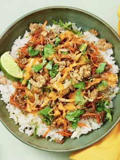 a green bowl filled with rice and meat on top of a yellow napkin next to a fork