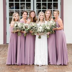 a group of women standing next to each other in front of a building holding bouquets