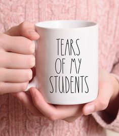 a person holding a white coffee mug with the words tears of my students on it