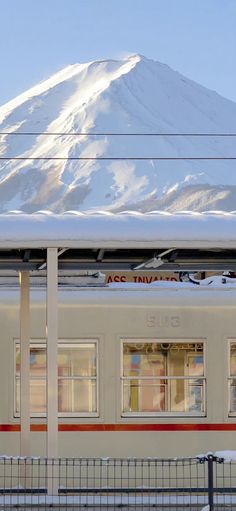 a train traveling past a snow covered mountain in the distance with power lines above it