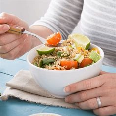 a woman is holding a fork and spoon over a bowl of food