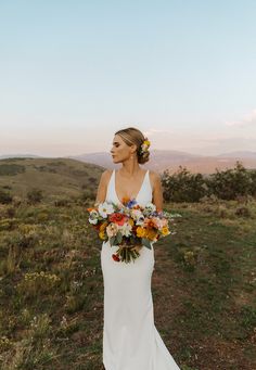 a woman in a white dress holding a bouquet of flowers on top of a hill