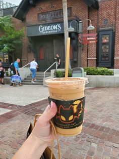 a person holding up a cup of coffee in front of a building with people walking by