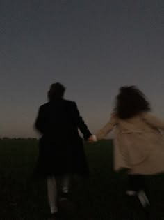 two people holding hands while walking across a field at night with the moon in the sky