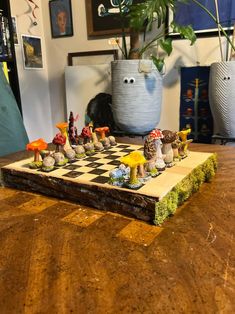 a wooden chess board with various figurines on top of it in front of a potted plant