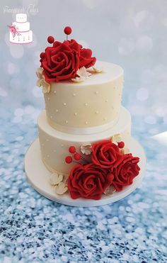 two tiered wedding cake with red roses on the top and white frosting, sitting on a blue tablecloth