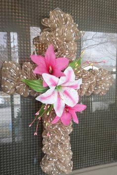 a cross decorated with pink flowers in front of a window